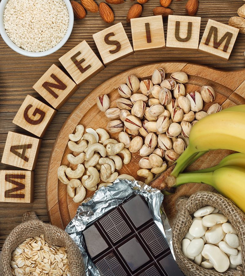Products containing magnesium bananas, pumpkin seeds, blue poppy seed, cashew nuts, beans, almonds, sunflower seeds, oatmeal, buckwheat, peanuts, pistachios, dark chocolate and sesame seeds on wooden table
