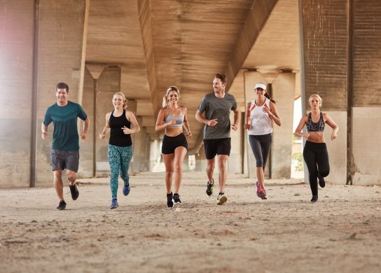 group of runners from running club under a bridge. Young men and women jogging together.