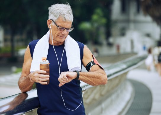 Senior jogger drinking water and checking application on his fitness tracker