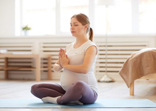 young pregnant woman doing yoga and meditating during workout at home, copy space