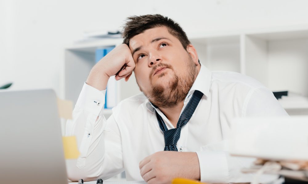 Image of a thoughtful fat businessman with laptop at workplace in office
