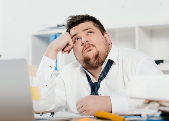Image of a thoughtful fat businessman with laptop at workplace in office