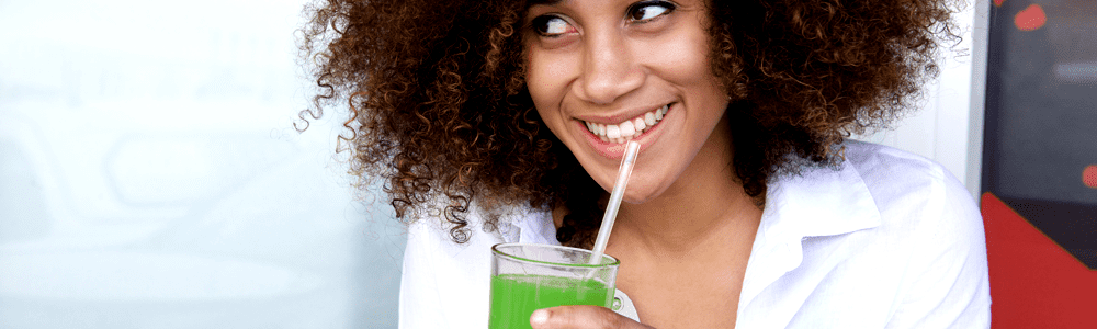 A woman drinking a green smoothie and smiling.