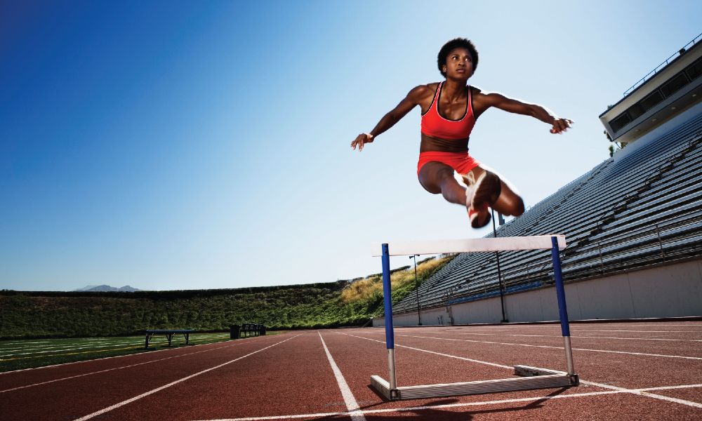 A woman jumping over a hurdle demonstrating sports performance exercise.