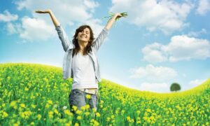 A happy, healthy looking woman in a field surrounded by yellow wild flowers.