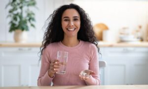 A beautiful woman smiling, getting ready to take a supplement with a glass of water