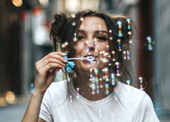 Young woman in a white T-shirt blowing colorful bubbles