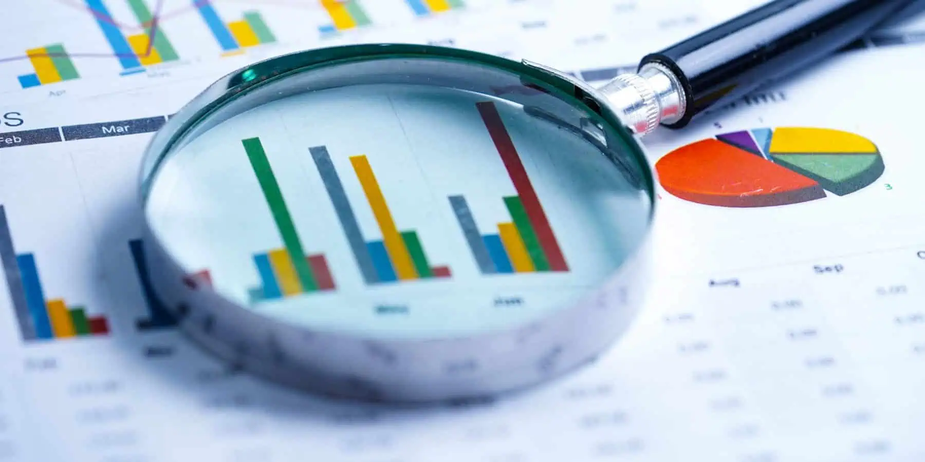 Magnifying glass on colorful financial charts and report.