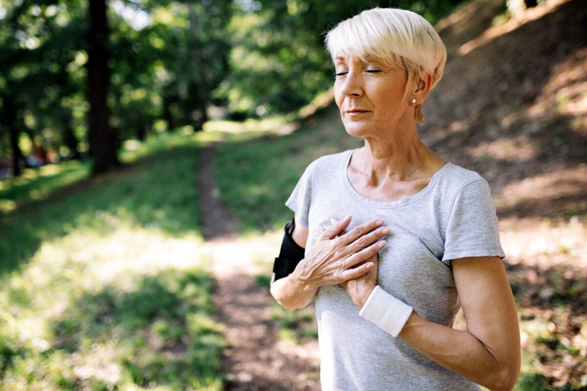 older woman on a hike holding her heart