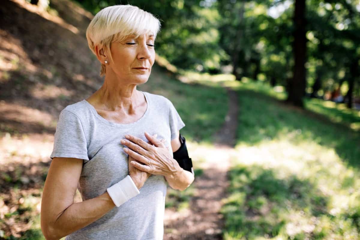 older woman on a hike holding her heart