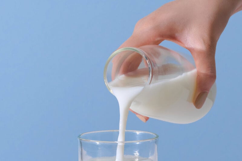 Pouring milk into glass with light blue backdrop.