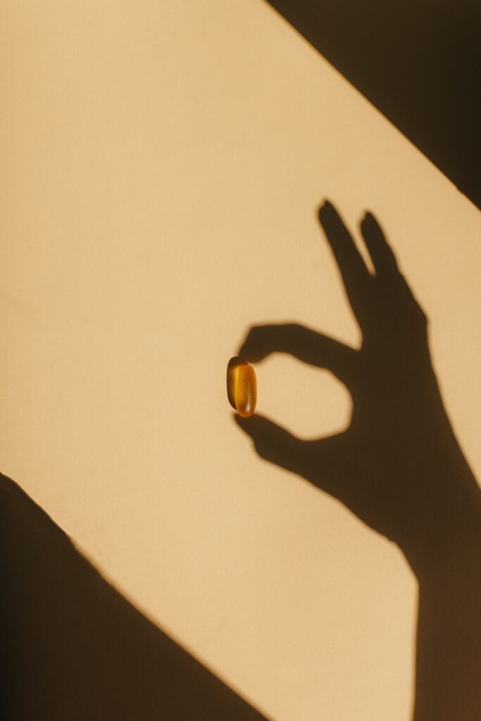 Hand shadow holdin g pill capsule Hands shadow makes okay sign over yellow capsule.