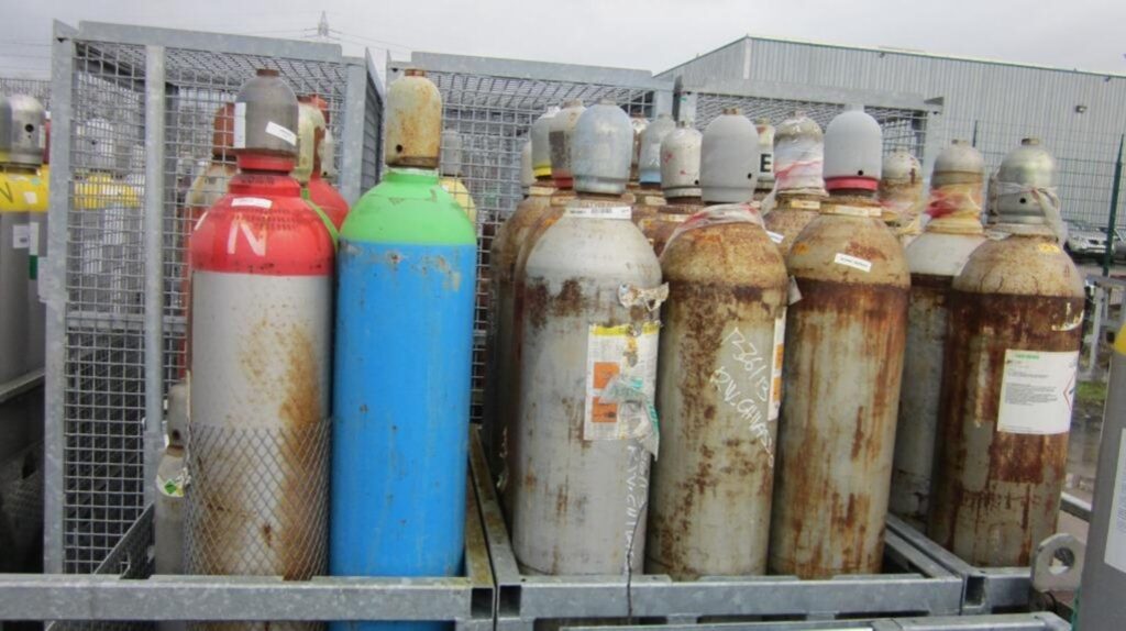 Rusty gas cylinders in metal cages outdoors.