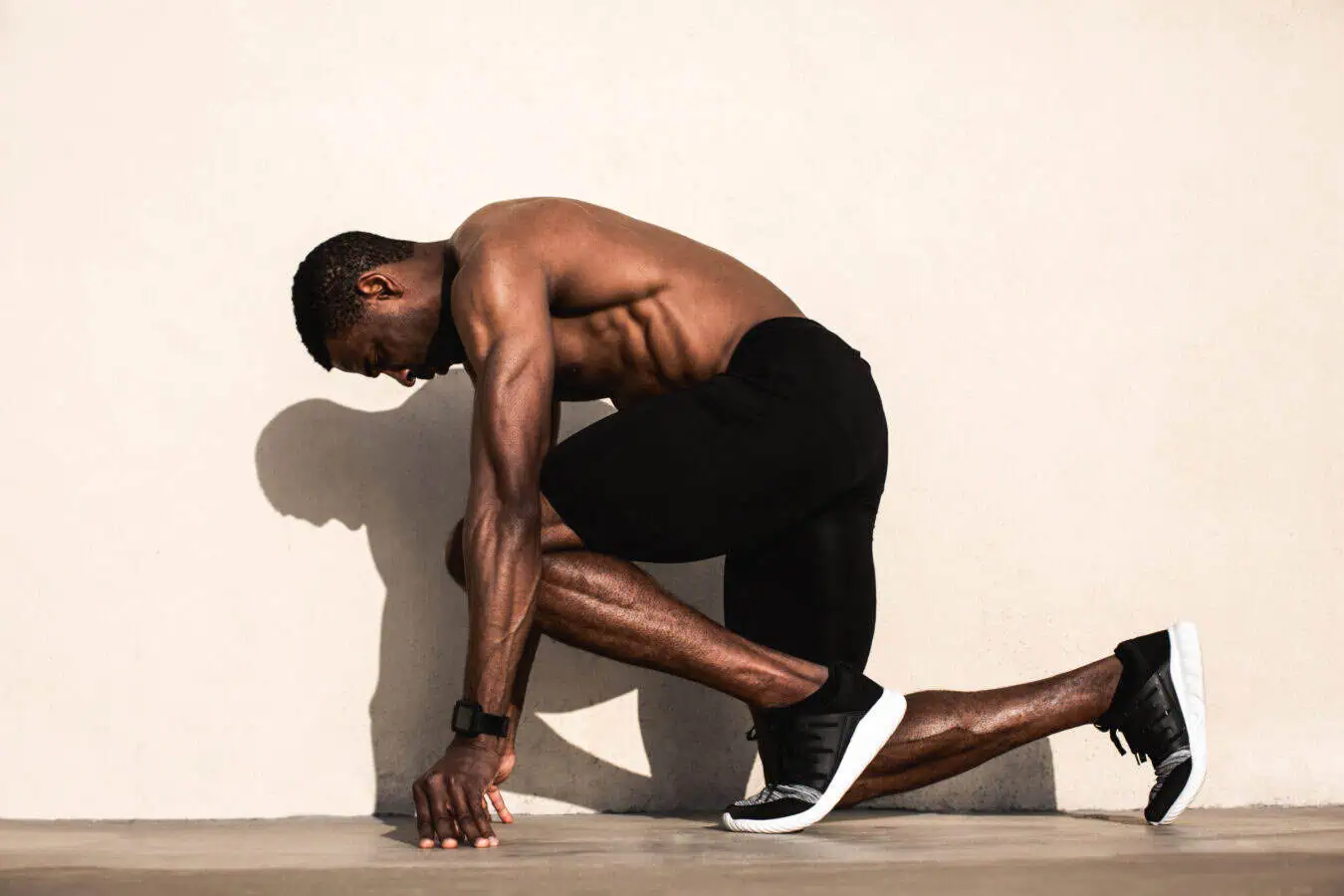 Shirtless person in shorts crouching by a wall.