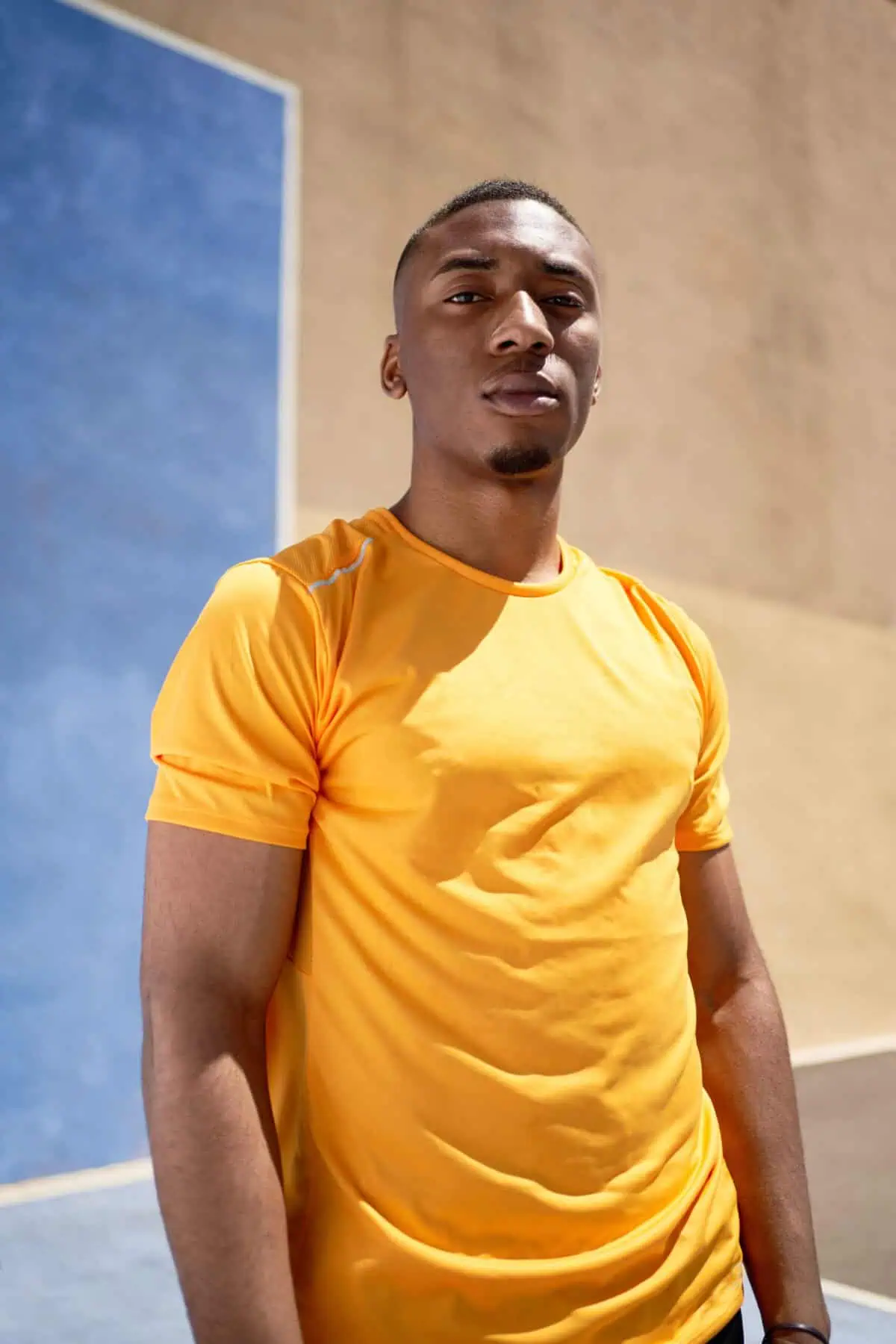 Person in yellow shirt by a blue and beige wall outdoors.