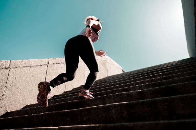 Runner on concrete stairs under clear sky.