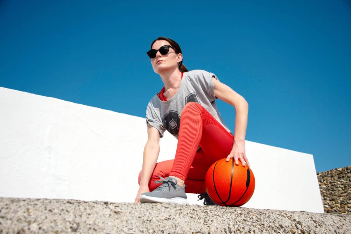 Female basketball player, holding a basketball, outside in the sun.