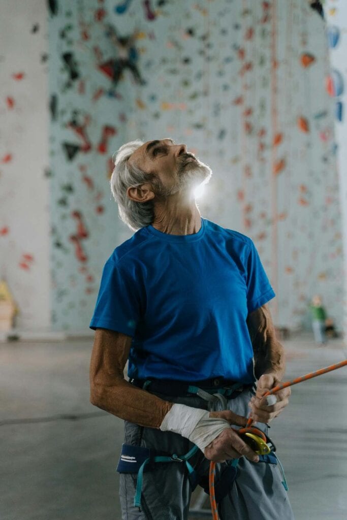 Older man in a shirt in front of a rock wall in a gym.