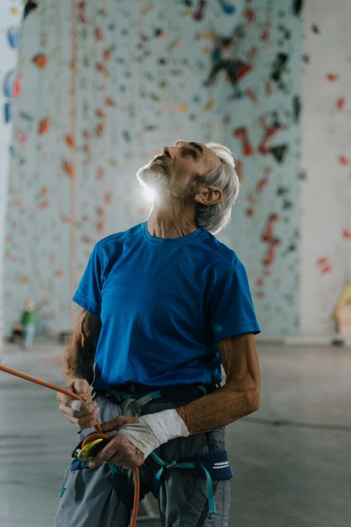 Older man in a shirt in front of a rock wall in a gym.