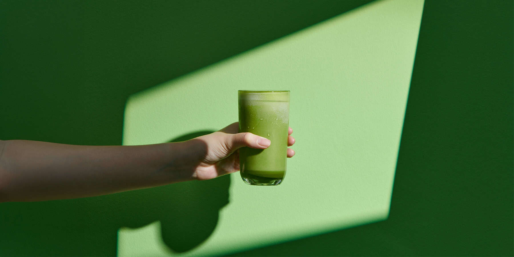 GLP 1 Nutritional Drinks Hero Image 1800x900px Green smoothie being held up on a green background