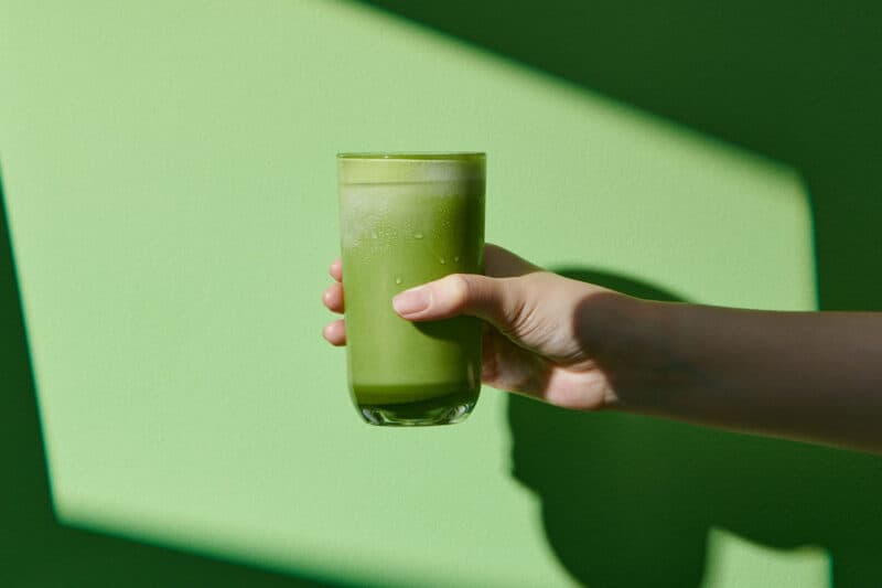 Image of a green smoothie being held out on a green background