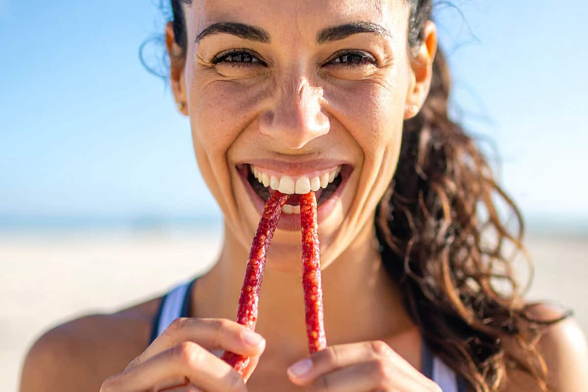 Protein Snack Image 1200x800px Image of a woman eating two meat snack sticks