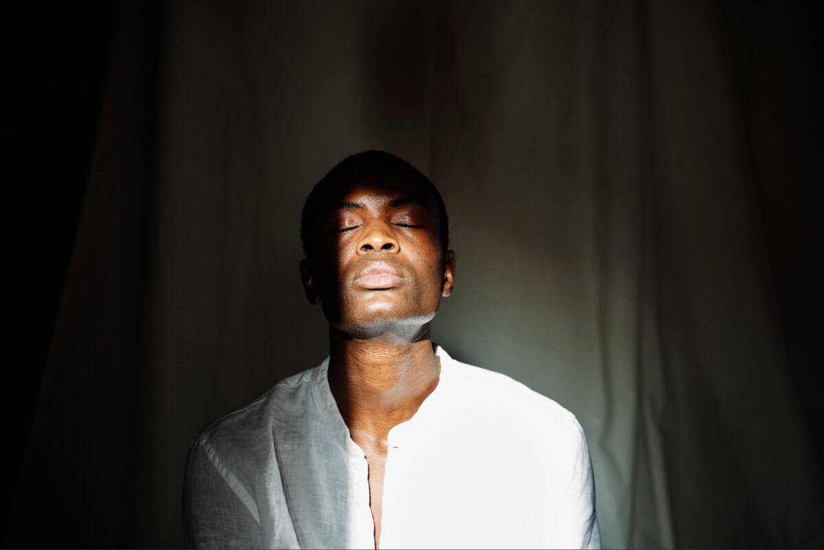 Image of a man sitting in a dark room with light hitting his face and chest.