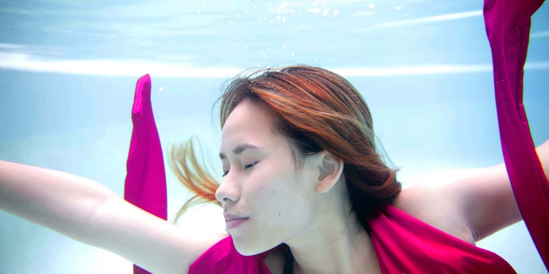 Image of a woman swimming in a pool with a pink scarf