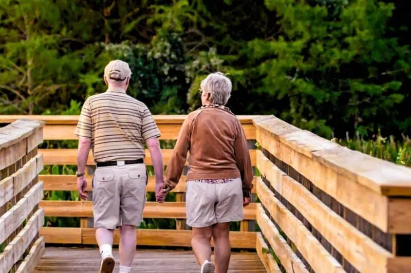 Image of two elderly people walking on a wooden bridge.