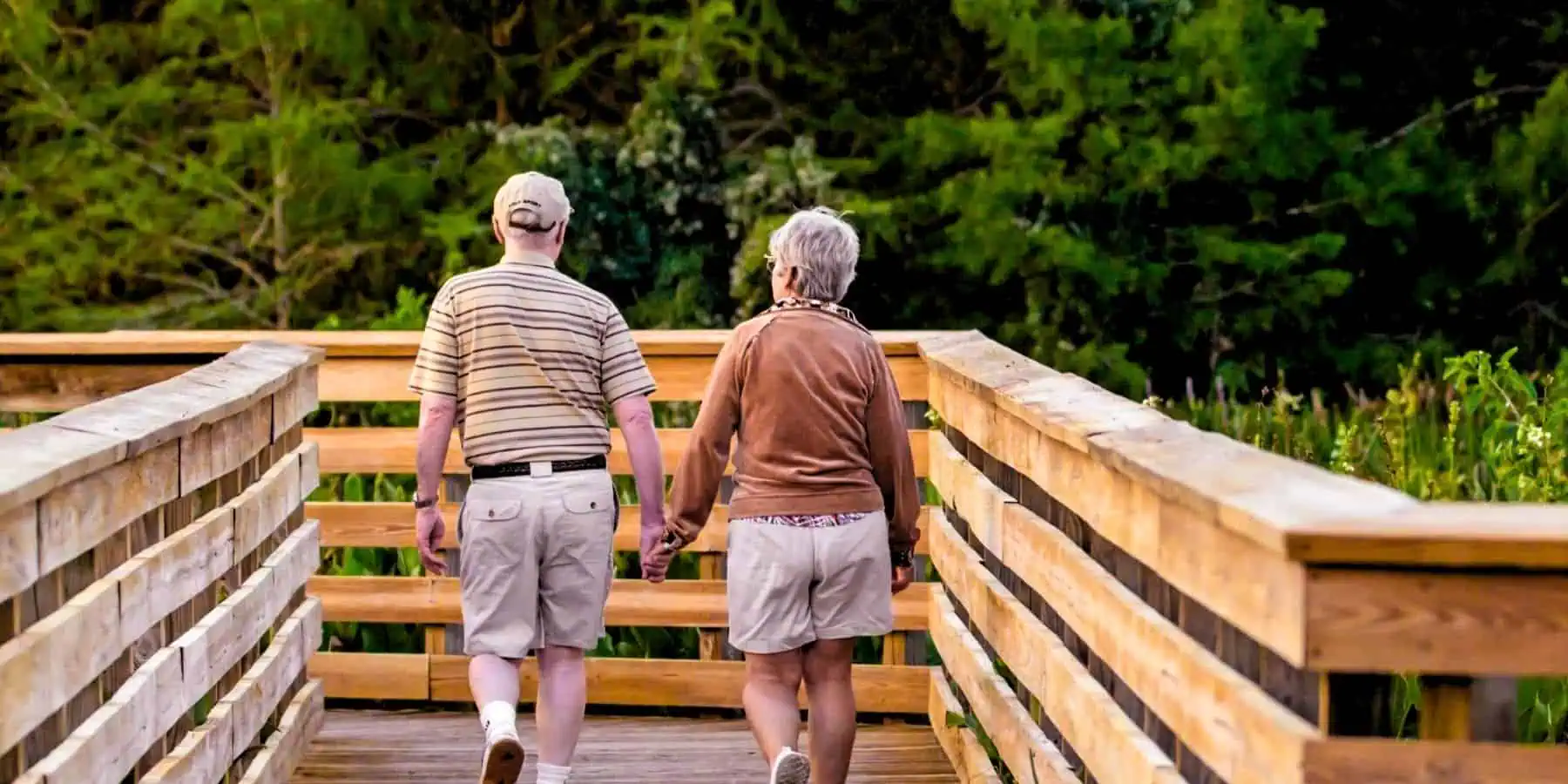 Image of two elderly people walking on a wooden bridge.