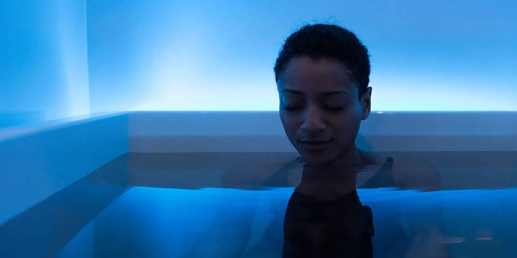 A woman immersed in a blue water environment representing whole-body wellness, cellular balance, and healthy biological processes.