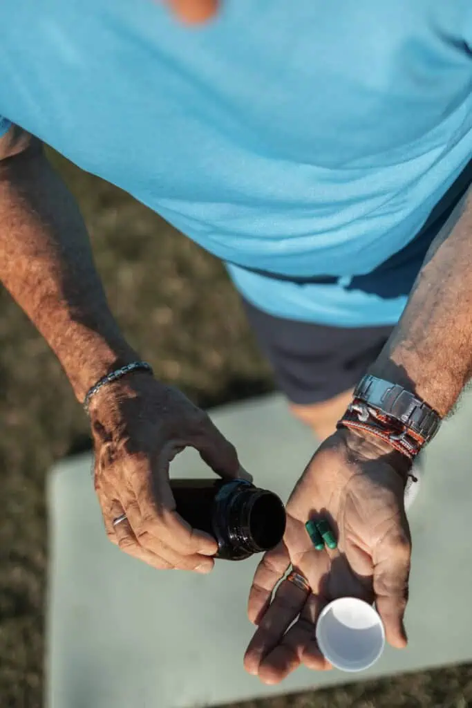 An individual handles pills from a container, depicting healthcare and wellness outdoors.