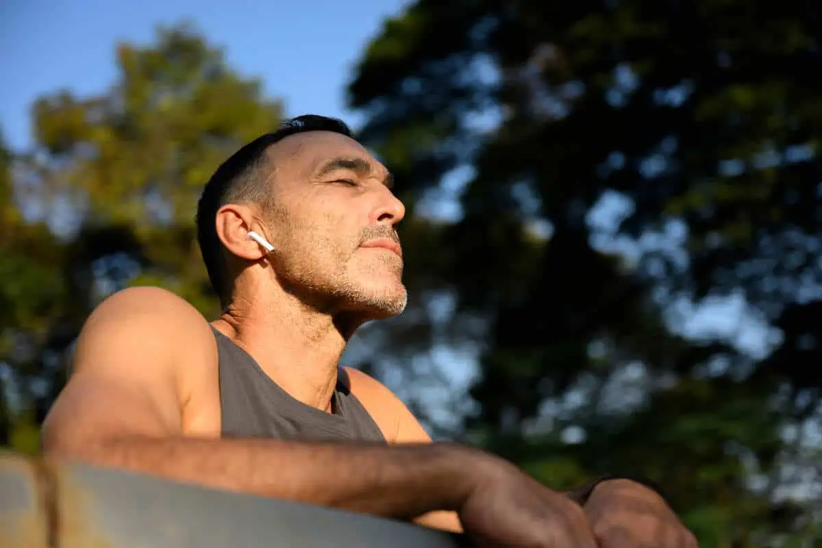 Person sitting outdoors in sunlight while wearing wireless earbuds