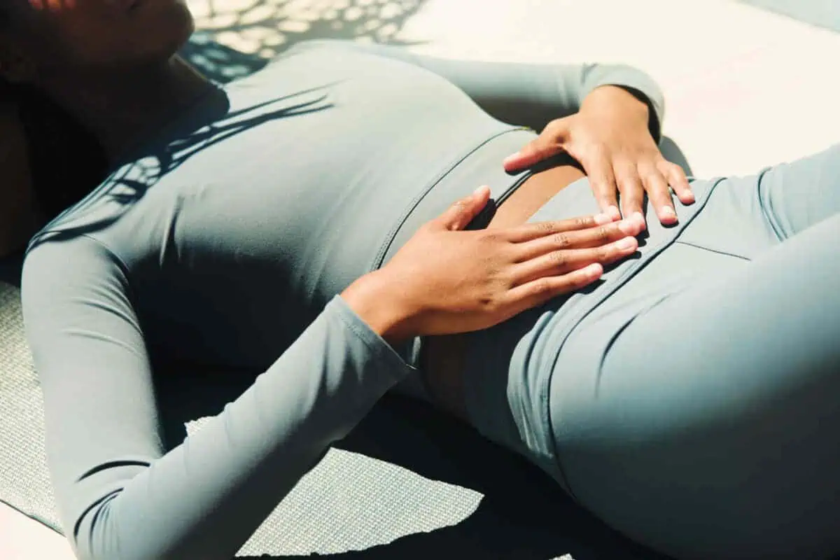 Person resting on an exercise mat with hands placed over the abdomen